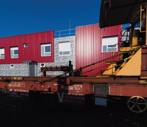 Bâtiment modulaire rouge ALGECO® près d'une voie ferrée avec wagon industriel