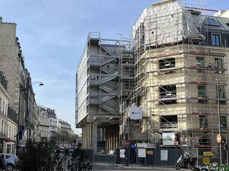 bungalows de chantier ALGECO® en base vie surélevée sur des colonnes contre un immeuble en travaux avec échafaudages en pleine ville