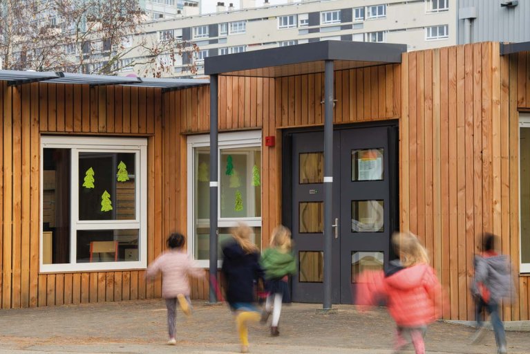 enfants courant vers l’entrée d’une école modulaire ALGECO® avec bardage bois et fenêtres décorées