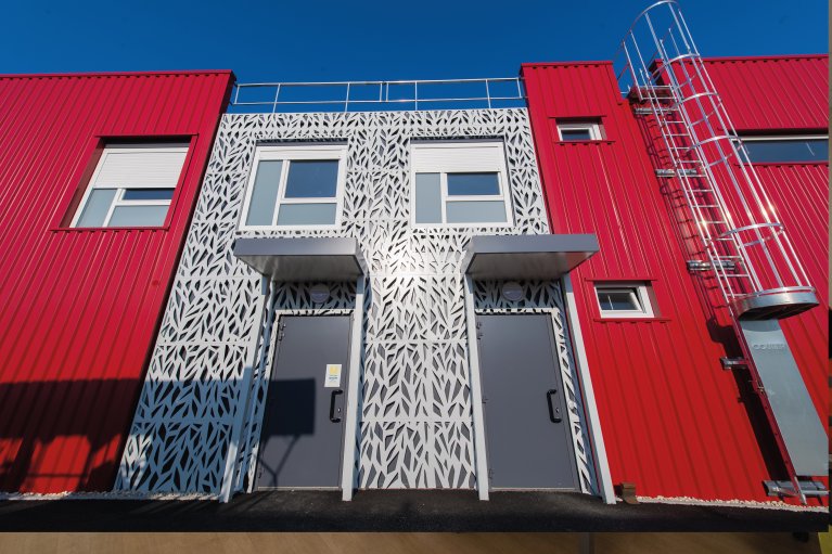 Façade de bureaux modulaires ALGECO® en métal rouge ondulée et décoration centrale en métal découpé argenté